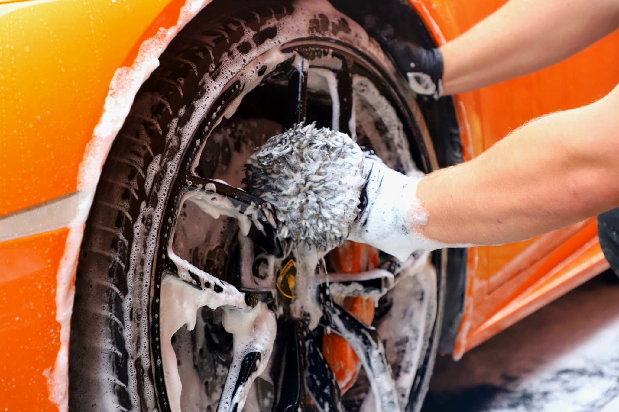 Lamborghini Huracan alloy wheel being cleaned with wash mitt and shampoo foam