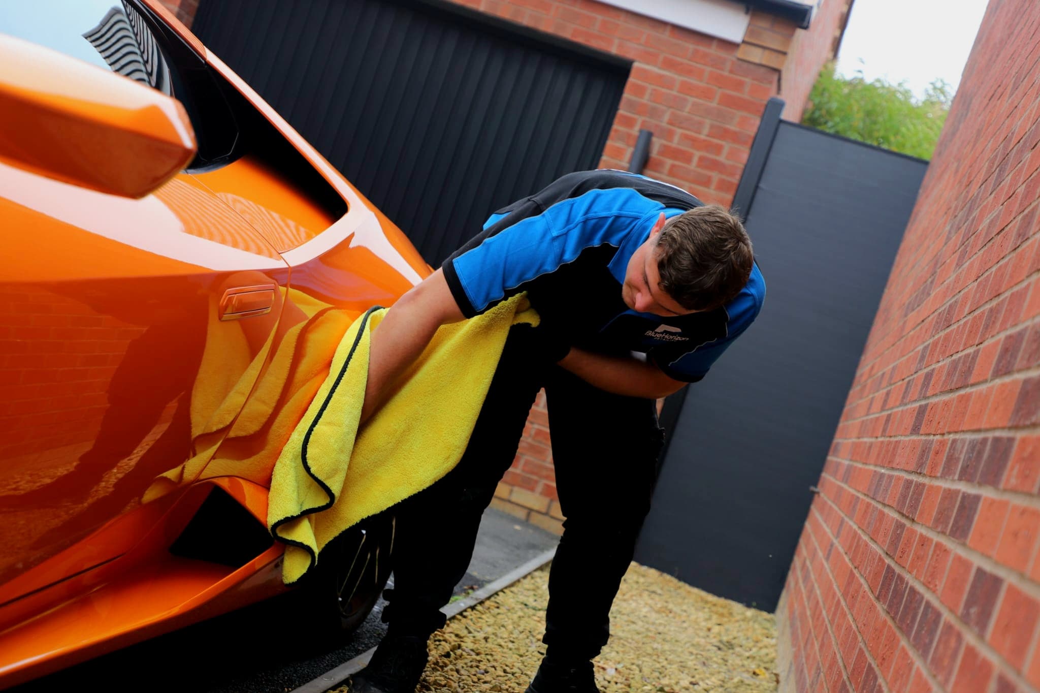 Drying the door panel of an orange Lamborghini Huracan with large yellow microfibre cloth after wash