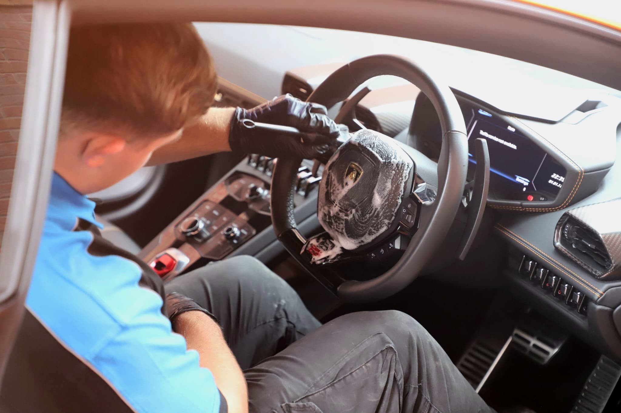 Interior cleaning of Lamborghini Huracan steering wheel with specialist cleaner and gloved hands