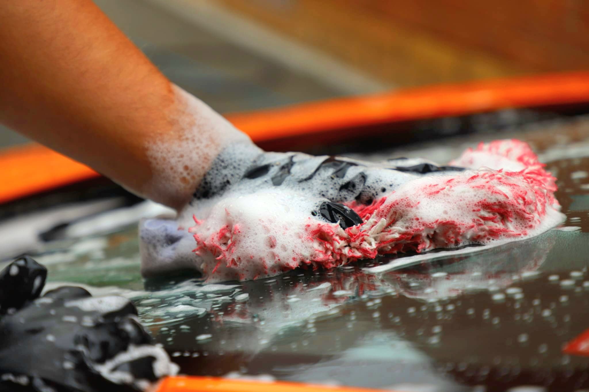 Close-up of wash mitt loaded with shampoo foam on Lamborghini Huracan paintwork during hand wash