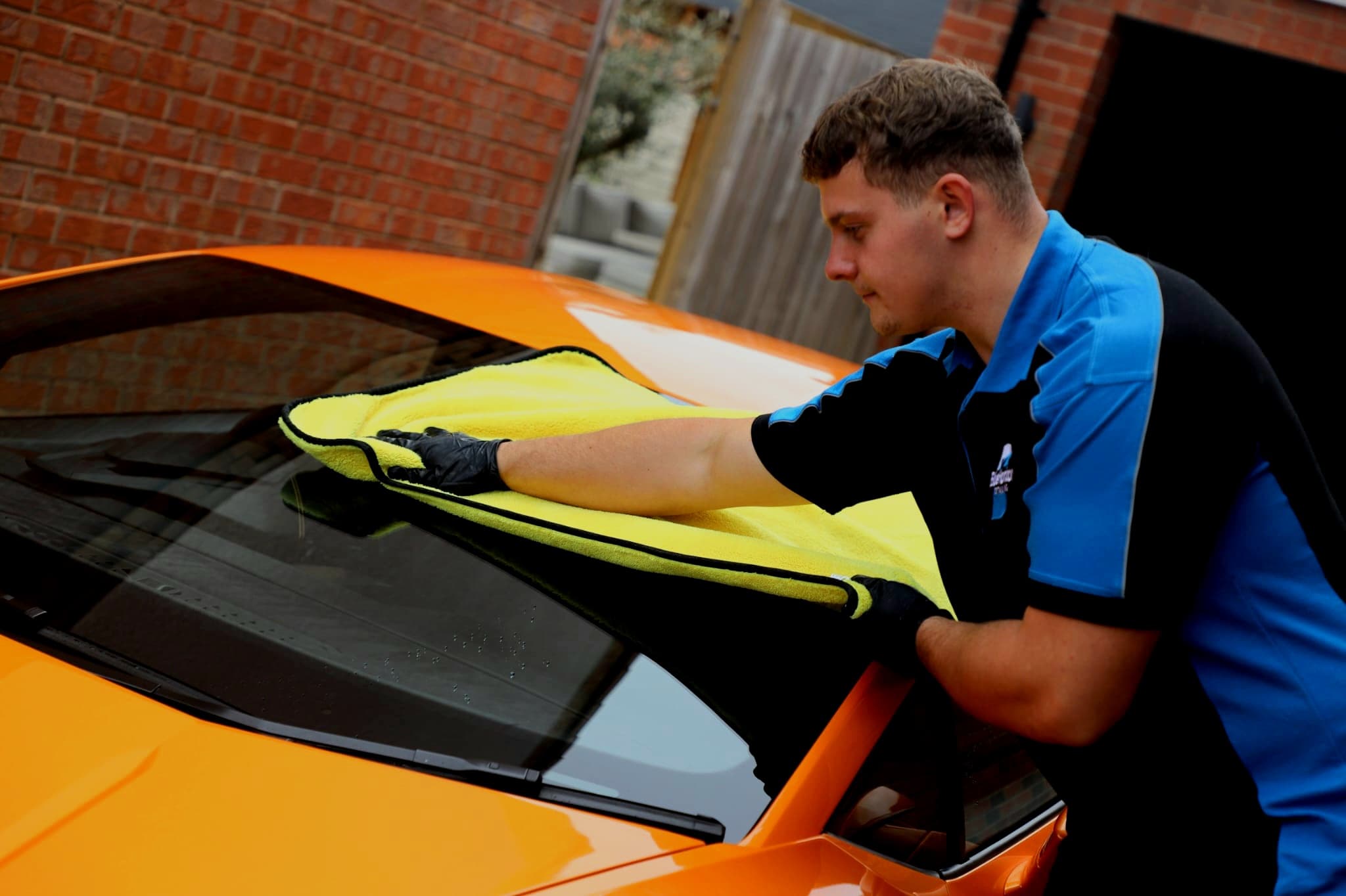 Detailer drying the windscreen of orange Lamborghini Huracan with yellow microfibre towel