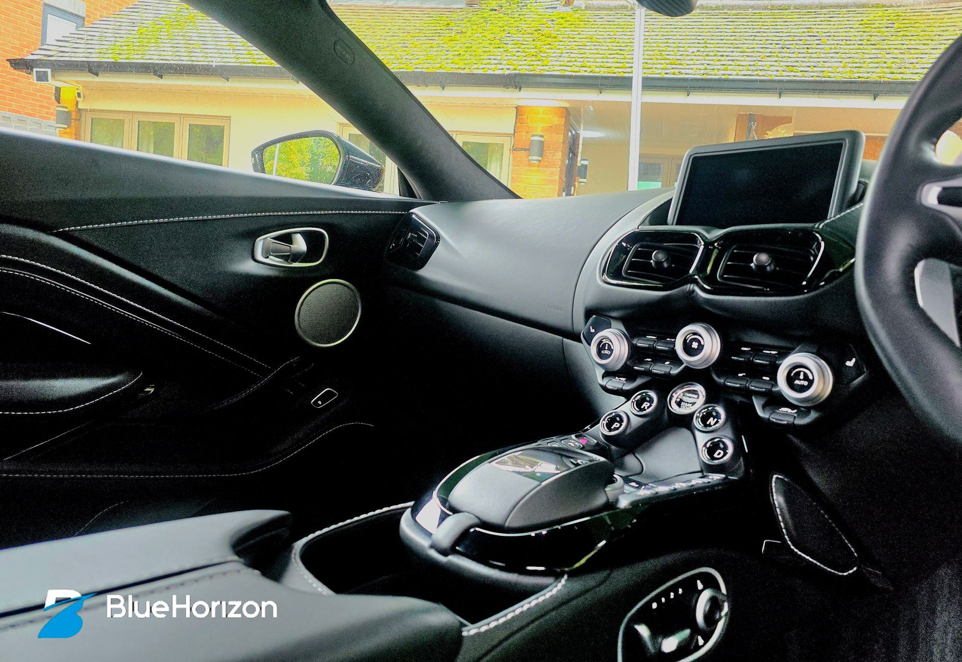 Interior view of a luxury car showing modern dashboard and controls, parked outside a house.