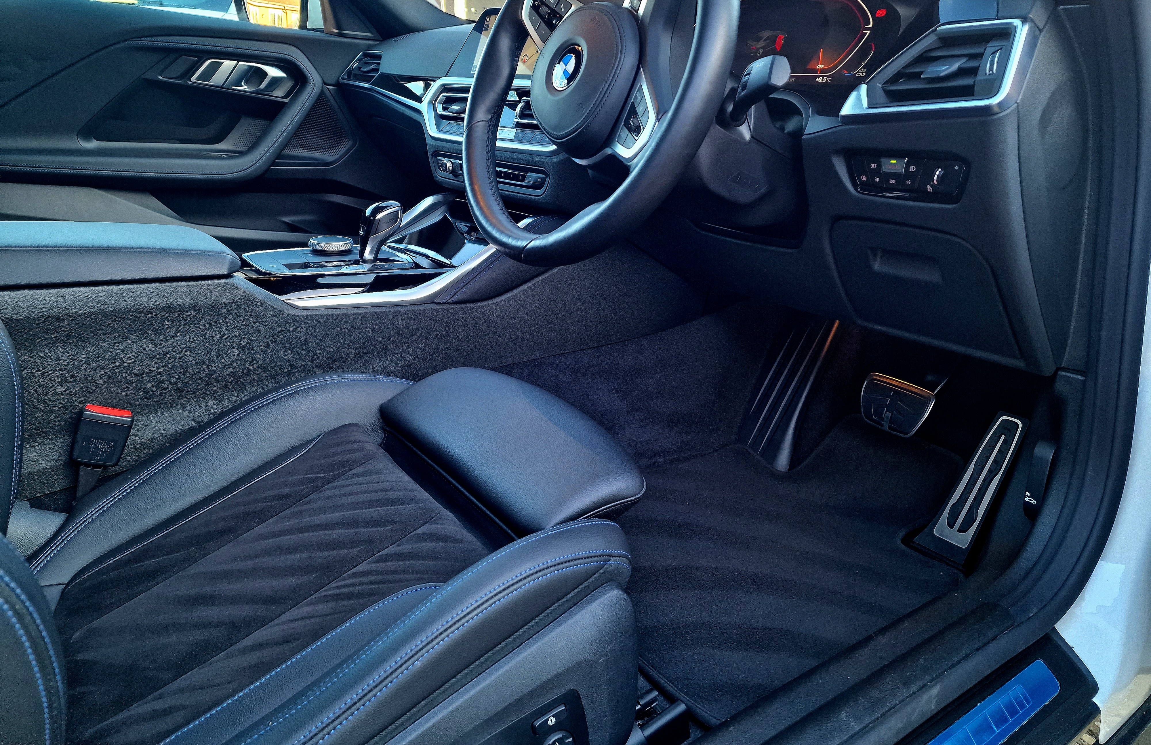 Interior of a modern car showing the driver's seat, steering wheel, dashboard, and foot pedals.