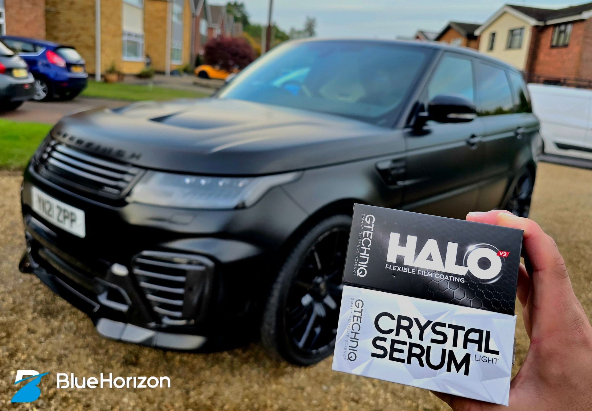 Hand holding car detailing products in front of a black SUV parked on a driveway.