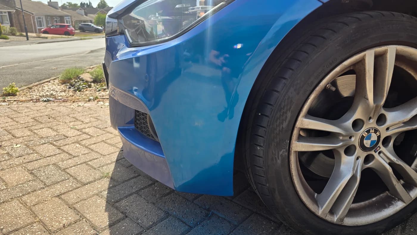 The same blue BMW bumper after repainting, with masking removed