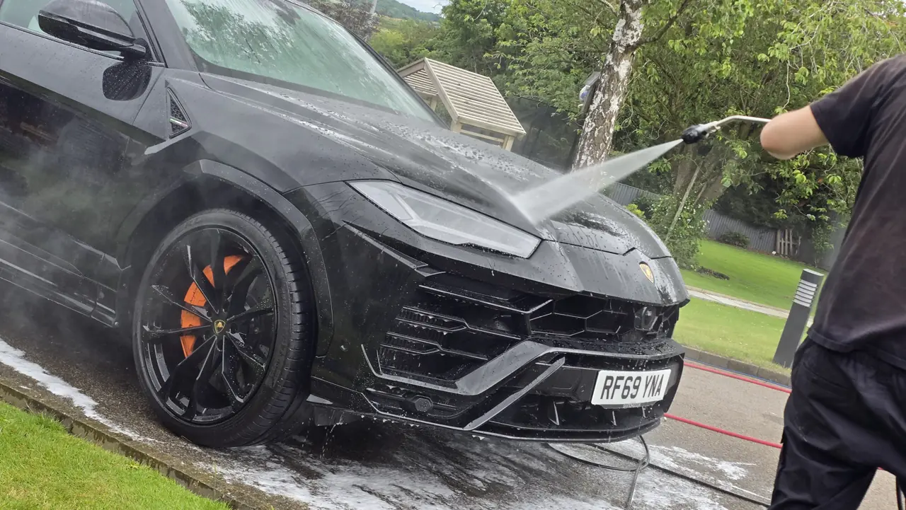 Blue Horizon detailer pressure washing a Lamborghini Urus on a customer driveway