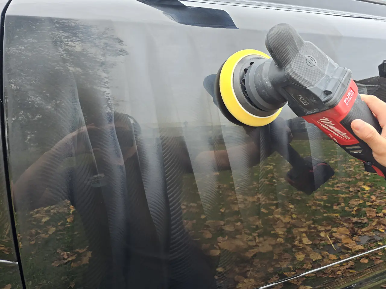 Machine polisher working across a real dark car panel during paint correction
